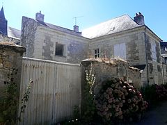 Photographie en couleurs d'une maison à étages en équerre derrière de hauts murs.