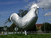 A large, shiny, metallic sculpture of a chicken facing right