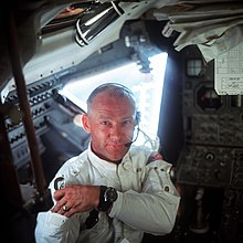 Photographie en couleur d'Aldrin dans le module de commande alors qu'il range ses lunettes dans une poche sur son bras.