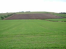 The western side of the battlefield, looking south-south-east from the monument erected in 1910. towards Branxton Hill on the skyline. The Scottish army advanced down the ploughed field, the English down the grassy field in the foreground. The modern boundary between the two fields marks the position of the marsh encountered by the Scots. Flodden Field (Braxton) - 2004-Feb-06 - Looking SSE from the monument.jpg