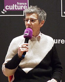 Une femme aux cheveux gris tenant un micro.