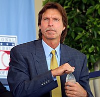 A man in a navy blazer, light blue shirt, and gold necktie