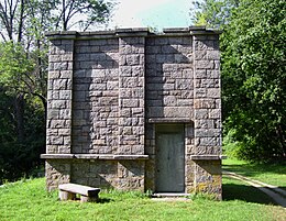 Small, square stone building with door and stone bench