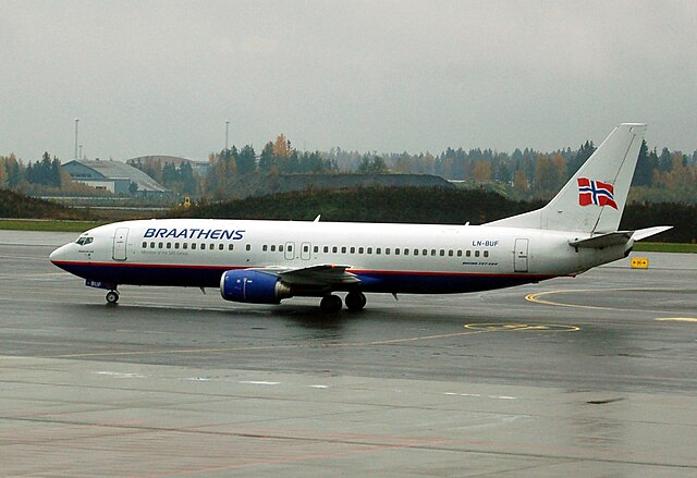 A medium-sized passenger jet on a tarmac with a white top and tail, and a blue bottom. There is a Norwegian flag on the tail and "Braathens" written along the side"