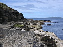 Útesy v zátoce Saviskaill Bay na severním pobřeží, v pozadí ostrov Westray