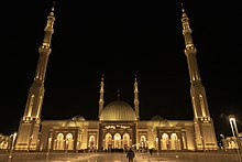 Photographie couleur d'une mosquée moderne dotée de quatre minarets, prise la nuit.