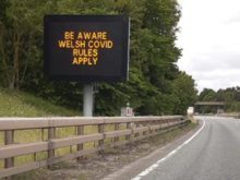 Sign indicating geographic differences in restrictions on the A55. Sign on the A55 near Queensferry at border between Wales and England 2 June 2020 (2nd crop).png