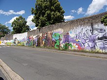 Photographie en couleurs d'une mur d'enceinte avec des contreforts et couvert de graffiti modernes.