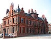 A two-storey brick building with extensive terracotta dressings and decoration; a steep grey slate hipped roof with a central attic and chimneys; each lateral bay protrudes slightly forward and is topped by a complex irregular gable end