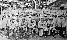 A black and white photograph of thirteen men arranged in two rows, standing and kneeling, on a baseball field. They are wearing light baseball uniforms with dark stripes and "Kingsport" written on the chest.