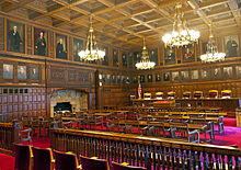 The courtroom seen above, empty but from a different angle showing more of it and its ornate walls, chandeliers and red carpet