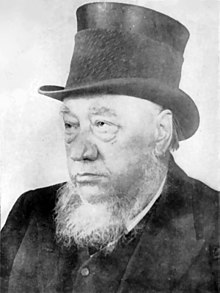 Paul Kruger as an old man with a grey beard wearing a black top hat as well as pirate style earrings