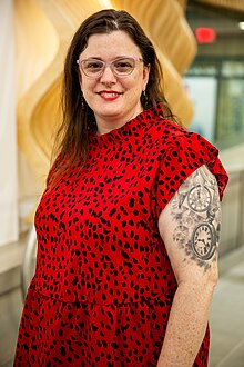 a white woman with a red top and an elaborate tattoo on her shoulder.