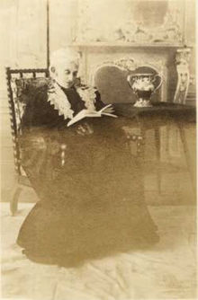 B&W photo of a sitting old woman who is reading.