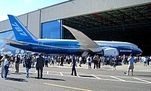 The Everett Factory Hall's huge door opens as the first 787 is rolled out. Surrounded the aircraft are guests and the public.