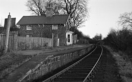 A black and white image of a single platform and single line with a stone built house on the platform