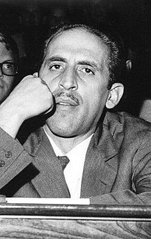 Image en noir et blanc du visage d'un homme appuyé sur son poing droit, regardant le spectateur.