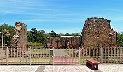 Photograph of masonry ruins behind a low fence on well-tended grounds