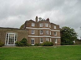 A three storey brown brick building with a cupola, and a single storey extension on the left, the foreground is a green lawn