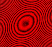 Fig. 2: Newton's rings interference pattern created by a plano-convex lens illuminated by 650 nm red laser light, photographed using a low-light microscope. The illumination is from above, leading to a dark central region. Newton's rings (650nm red laser light).jpeg