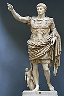 A marble statue of the Emperor Augustus. He stands with one arm raised as if in command. Augustus is portrayed as a man of about thirty five, with short hair and clean shaven. He wears Roman military uniform of a breast plate, leather accoutrements and a cloak over a short tunic. The breastplate is decorated with symbolic figures. As a work of art, the statue displays high technical mastery.