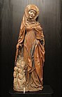 Photographie d'une statue de sainte en bois polychrome, représentant sainte Marthe enveloppée d'un manteau qui couvre des pénitents groupés à ses pieds