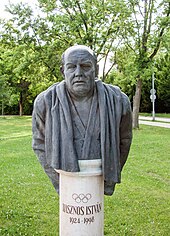 Büste von István Hasznos auf einer Stele. Deutlich erkennbar ist der Bademantel und das um den Hals hängende Handtuch.