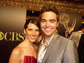 A man with dark hair wearing, a brown suite also accompanied with a brunette hair woman wearing a red outfit.