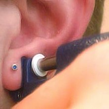 An ear being pierced with an ear-piercing instrument Earpiercing.jpg