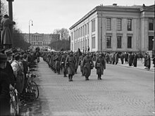 Des soldats défilent dans une rue sous les yeux de la foule.