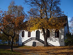 Vitrappad byggnad med tegeltag. Mitt på fasaden en trappa mot en välvd dörr. Dörrar och fönster ger intryck av kyrka, i övrigt en neutral byggnad.