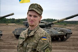 A Ukrainian soldier in standard camouflage dress with tanks in the background