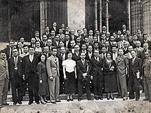 Photographie en noir et blanc d'un groupe d'hommes et de femmes posant sur des marches.