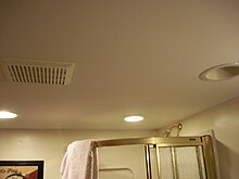 Picture of a bathroom ceiling, with a vent, light, and the top of a shower in the background