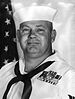 A black and white image showing the head and upper torso of Williams wearing his military dress uniform with hat and ribbons. An American flag is visible in the background