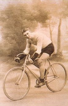 Photographie en sépia d'un cycliste courbé sur son vélo, portant un maillot blanc et un cuissard noir.