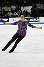 A photograph of Nathan Chen performing on the ice in a colourful shirt.