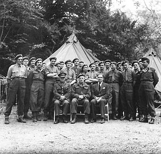 Photograph of a group of uniformed soldiers seated and standing in front of a tent