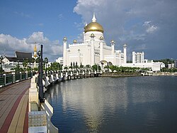 Большая белая мечеть с золотым куполом у воды.