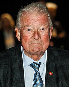 Foto eines älteren Mannes, der einen Anzug mit einem apfelförmigen FrP-Ansteckbutton trägt