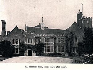 Black and white photograph of H-plan red brick tudor house with a porch on the left, two decorative oriels on the right, and a tall Tudor tower in the background connected to the building.