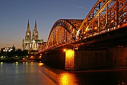 Laat skemer in Keulen, Duitsland. In die voorgrond is die Hohenzollern-spoorwegbrug, met die Katedraal van Keulen in die agtergrond en die Museum Ludwig aan sy linkerkant.