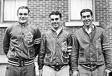 three young men stand side by side. Each has short, dark hair parted in the middle and are wearing identical team jackets with a stylized maple leaf logo on the left breast.