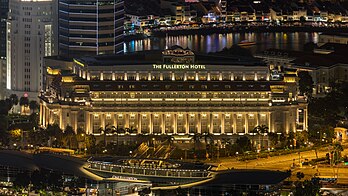 Vista do hotel The Fullerton à noite com luzes coloridas refletidas na água (visto da plataforma de observação do Marina Bay Sands). O Fullerton Hotel Singapore é um hotel de luxo cinco estrelas localizado próximo à foz do rio Singapura, no centro da área central de Singapura. Encomendado em 1924 como parte das comemorações do centenário da colônia britânica, o edifício foi projetado como um prédio de escritórios. Em 1997, foi convertido em hotel e construído um complexo comercial de dois andares, o One Fullerton. As obras de renovação do Edifício Fullerton foram concluídas em 8 de dezembro de 2000. O hotel foi inaugurado oficialmente pelo então primeiro-ministro Goh Chok Tong em 1 de janeiro de 2001. Em 2015, foi declarado monumento nacional de Singapura. (definição 6 107 × 3 435)