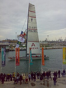 un bateau à voile vu de la gauche, dans le chenal d'un port