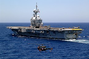 Photographie couleur montrant le porte avion français Charles de Gaulle en cours de catapultage d'avions super-étendard. La vue de trois quart arrière à gauche, permet de voir l'alouette III en premier plan qui surveille les envols.