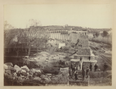 Photographie en sépia montrant la construction des dernières piles du pont et les ouvriers du chantier, la courbe fait que le viaduc fuit vers la gauche de l'image.