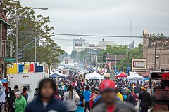 A large street festival in Milwuakee, Wisconsin. Much of the crowd is African-American, and cooking smoke can be seen rising from food trucks and stands parallel to the street.