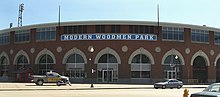 Большой кирпичный стадион с множеством круглых окон внизу и множеством прямоугольных окон в группах по четыре выстроенных вверху стадиона. Над дверью изображены слова Modern Woodmen Park.