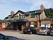 A speckled building with a rectangular, dark blue sign reading "NORTH EALING STATION" in white letters all under a blue sky with white clouds